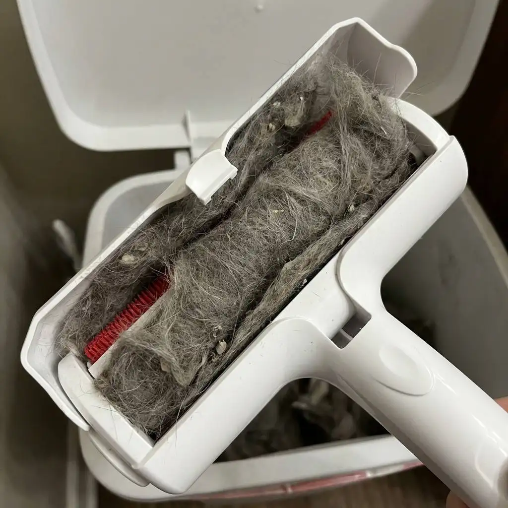 Top view of an open compartment overflowing with a dense, matted roll of grey cat fur and dust.